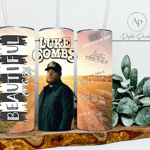 Könnte beinhalten: Drei Edelstahlbecher mit unterschiedlichen Designs. Der erste Becher hat den Text "BEAUTIFUL crazy" in Schwarzweiß. Der zweite Becher hat ein Foto von Luke Combs und den Text "LUKE COMBS". Der dritte Becher hat den Text "BEER NEVER BROKE MY HEART" und "Better Together" in Schwarzweiß. Die Becher stehen auf einer Holzoberfläche.