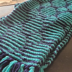 May include: A teal and navy blue knitted scarf with fringe on the ends.