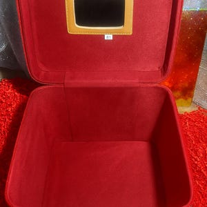 Può includere: Custodia per trucco rossa aperta con uno specchio rettangolare incorniciato in beige. Anche l'interno è rosso. Il numero "81" è stampato su una piccola etichetta bianca sotto lo specchio. La custodia è su una superficie rossa.
