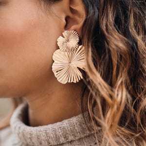 Könnte beinhalten: Ohrringe in Goldton mit einem mehrschichtigen Blumendesign. Die Ohrringe sind aus Metall und haben eine strukturierte Oberfläche.