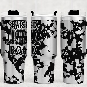 May include: A stainless steel tumbler with a black and white splatter pattern. The tumbler has a black lid and handle. The text "Raised on an old dirt road" is printed on the side of the tumbler.