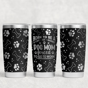 May include: Three stainless steel tumblers with black and silver paw print and bone designs. The center tumbler has the text "BORN TO BE A STAY-AT-HOME DOG MOM forced TO GO TO WORK".