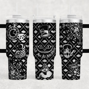 Op de afbeelding: Een zilveren roestvrijstalen tumbler met een zwart-wit ontwerp met personages en symbolen uit Alice in Wonderland. De tumbler heeft een zwarte handgreep en een rietje. Het ontwerp bevat een klok, een theekopje, een Cheshire Cat, een Hoedenmaker, een theepot en de woorden "We Are All Mad Here".