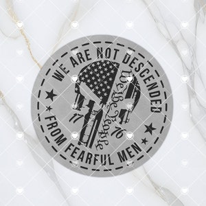 以下が含まれることがあります： アメリカの国旗のデザインのヘルメットをかぶった頭蓋骨の黒いシルエットが描かれた、灰色の丸い金属製の看板。看板には「We Are Not Descended From Fearful Men」という文字が書かれており、文字の両側に星が1つずつある。頭蓋骨のヘルメットには「We The People 1776」という文字が書かれている。