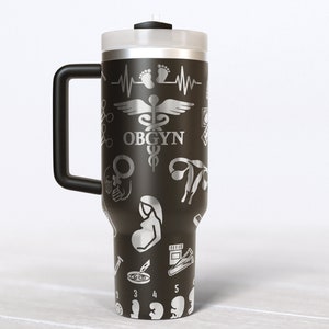 May include: Black stainless steel travel mug with a black handle. The mug is covered in a pattern of silver medical symbols, including a caduceus, a stethoscope, a heart rate monitor, and a pregnant woman. The text "OBGYN" is printed on the mug.