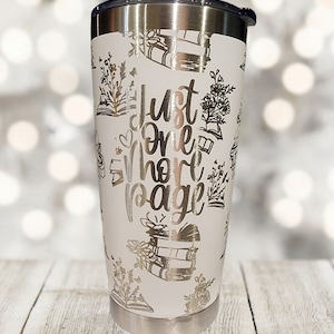 May include: White stainless steel tumbler with a silver design of books and flowers. The text "Just one more page" is printed on the tumbler.
