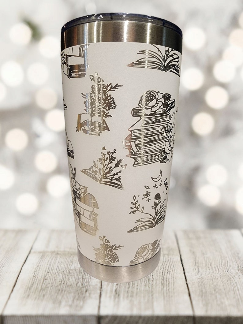 May include: White stainless steel tumbler with a silver metallic design of books, flowers, and moons.