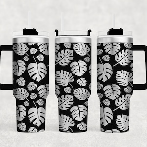 May include: A stainless steel tumbler with a black and silver tropical leaf pattern. The tumbler has a lid, a handle, and a straw.