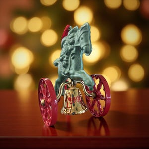 Op de afbeelding: Een kerstversiering met een groene paardenkoets met rode wielen en een gouden bel. Het paard draagt een rode kerstmuts. De versiering staat op een donkerrood oppervlak met een vage achtergrond van gele lichten.