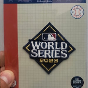 May include: A blue and gold World Series patch with the MLB logo and the year 2023. The patch is on a white background with a grid pattern.