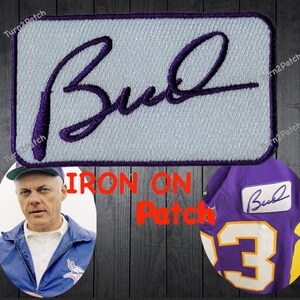 May include: Purple and white iron-on patch with the signature "Bud" in purple thread. The patch is shown on a purple jersey with the number 3.