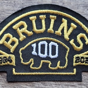 May include: A black and gold embroidered patch with the word "BRUINS" in gold lettering and the number "100" in white lettering. The patch also includes the years "1924" and "2024" in gold lettering.