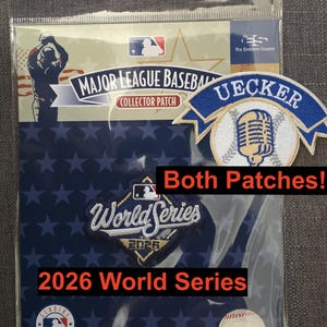 May include: Two embroidered patches in a clear plastic sleeve. One patch is a blue and white Uecker design with a microphone and baseball. The second is a diamond-shaped 2026 World Series patch with blue, white, and gold embroidery. The packaging features Major League Baseball branding and a holographic sticker.