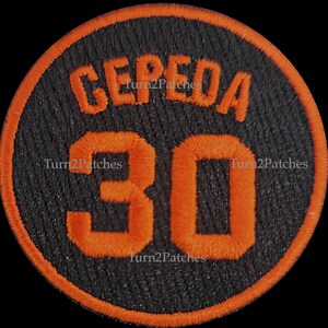 May include: A black and orange embroidered patch with the name "CEPEDA" and the number "30" in a circle.