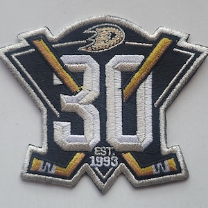 May include: A black and white embroidered patch with a hockey stick design. The patch features the number 30 and the text "EST. 1993".