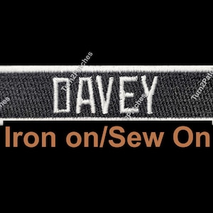May include: Black rectangular patch with the name "DAVEY" embroidered in white block letters. The patch has a white border and the text "Iron on/Sew On" in brown below the name. The background is black.