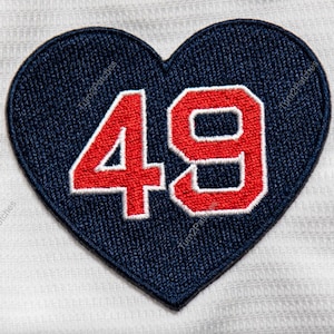 May include: A blue heart-shaped patch with the number 49 in red with white outlines. The patch is embroidered.