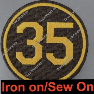 May include: A circular patch with the number 35 in yellow, centered on a dark brown background. The number is outlined in yellow, and the patch has a yellow border. The text "Iron on/Sew On" is at the bottom.