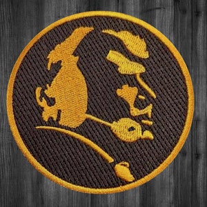 May include: A round, black embroidered patch with a gold silhouette of a person's head and shoulders. The person's face is turned to the side and their hair is styled in a short, wavy bob.