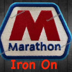 May include: Embroidered patch with a white, blue, and red design. The patch features a large red "M" inside a white hexagon shape, with the word "Marathon" below. The text "Iron On" is written in red at the bottom.