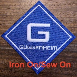 May include: A blue diamond-shaped iron-on or sew-on patch with a white "G" and the text "GUGGENHEIM" in white.