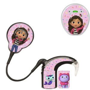 Puede incluir: Un procesador de implante coclear negro con bobina, con un fondo rosa y chispas de colores. El dispositivo muestra un personaje de dibujos animados con cabello castaño rizado y orejas de gato, junto a un gato sirena y un gato morado.