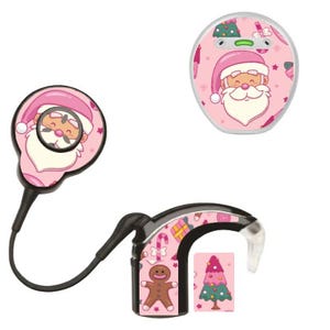 Puede incluir: Dispositivos de audífonos rosas y negros con temática navideña. Los dispositivos presentan a Papá Noel, hombres de jengibre y árboles de Navidad. Los componentes del audífono están conectados por un cable negro.