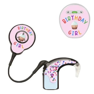Könnte beinhalten: Rosa Hörgeräte-Zubehör mit dem Schriftzug "BIRTHDAY GIRL" und einem Cupcake-Motiv. Eines ist rund, das andere hat ein schwarzes Kabel und eine Hörgerätekomponente mit bunten Konfetti.