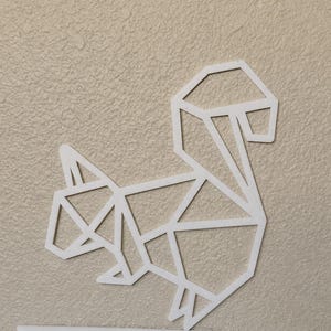 May include: A white wall-mounted decoration shaped like a squirrel, constructed from thin, flat geometric lines that form a stylized, angular outline of the animal. The design features a prominent, curved tail and a distinct head and body shape.
