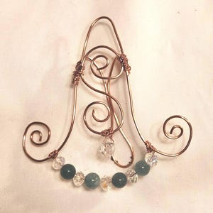 Puede incluir: Un peine para el cabello de alambre de cobre con un diseño decorativo de espiral y una fila de cuentas verdes y transparentes.