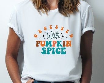 May include: White t-shirt with the text "OBSESSED With PUMPKIN SPICE" in a retro font with orange, brown, and teal colors. The text is surrounded by small stars.