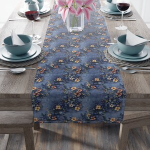 May include: A blue floral table runner with a distressed look. The runner features a repeating pattern of small pink, yellow, and orange flowers on a blue background. The runner is 14 inches wide and 70 inches long.