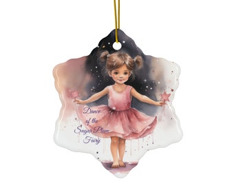 May include: A ceramic snowflake ornament featuring a watercolor illustration of a young girl in a pink dress, holding a star wand. The text "Dance of the Sugar Plum Fairy" is written in purple below the girl.