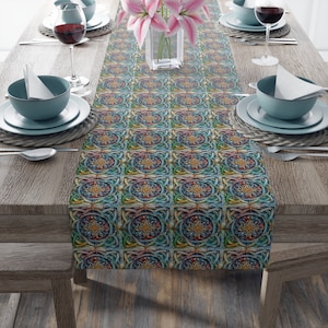 Puede incluir: Un camino de mesa colorido con un patrón geométrico repetitivo en tonos azules, verdes, amarillos y naranjas. El camino de mesa está colocado sobre una mesa de madera preparada para una comida, con platos, cuencos y vasos.