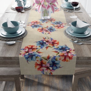 Könnte beinhalten: Ein beiger Tischläufer mit einem floralen Muster aus roten, rosa und blauen Blumen. Der Läufer liegt auf einem Holztisch mit zwei Gedecken auf jeder Seite.