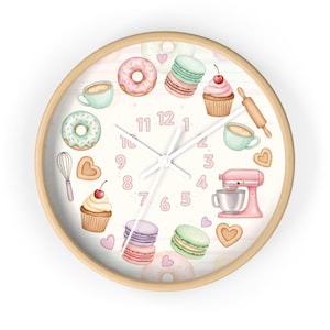 May include: A round wall clock with a light wood frame. The clock face features a whimsical design of baked goods, including donuts, cupcakes, macarons, and a pink stand mixer. The numbers are in a soft pink color.