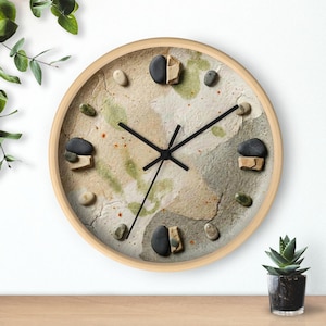 May include: Round wall clock with a light wood frame. The clock face has a textured, neutral-toned background with black clock hands. Small stones and pebbles are used as hour markers, adding a natural, earthy aesthetic.
