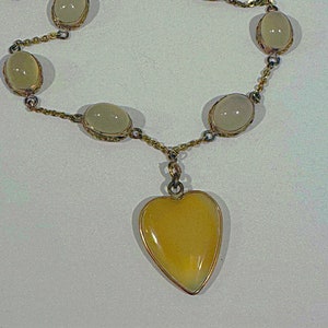 May include: A gold chain necklace with a heart-shaped pendant and oval-shaped stones. The stones are a pale yellow color.