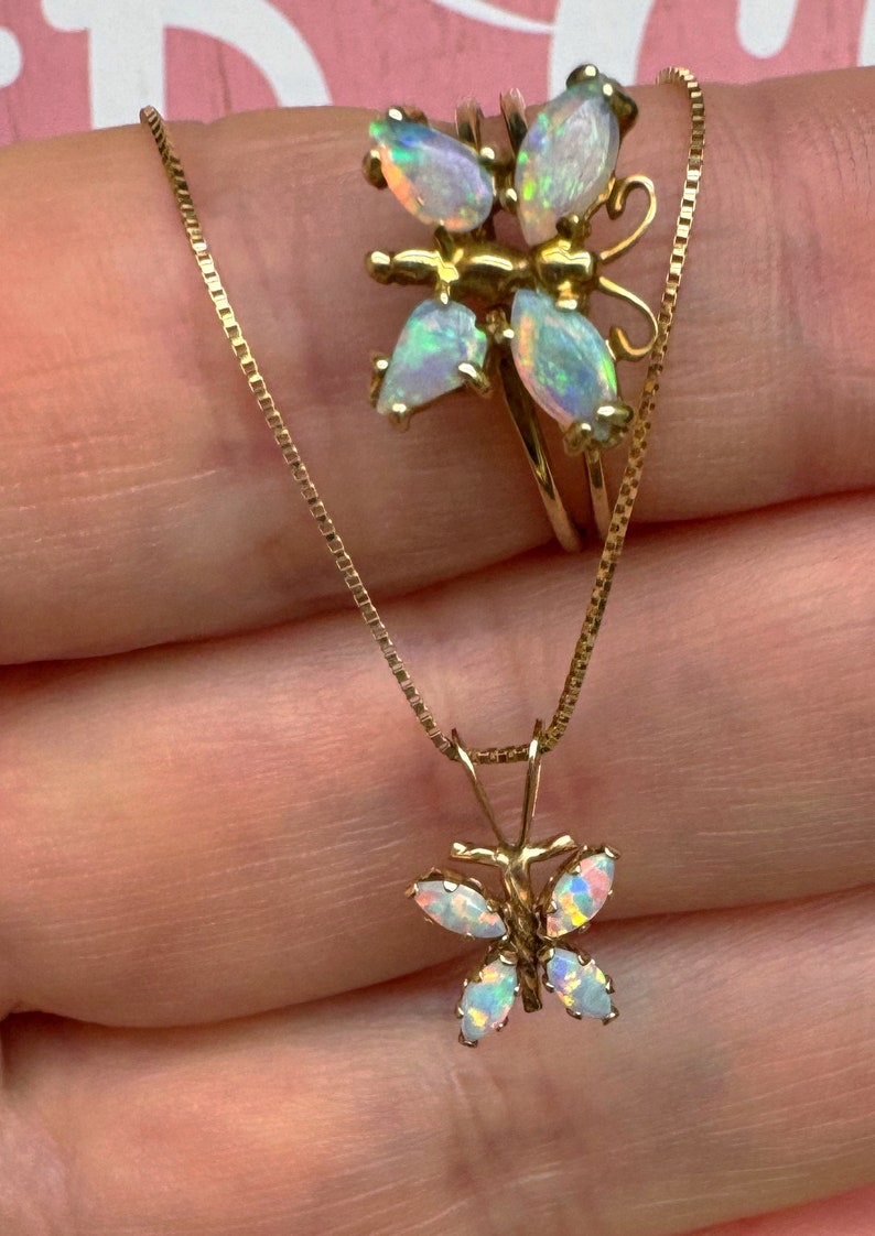 May include: A gold chain necklace with a butterfly pendant. The butterfly is made of opal stones and has a delicate design. The chain is a box chain style.