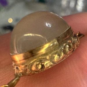 May include: A gold-toned pendant with a large, clear, round, faceted gemstone. The pendant has an ornate, detailed design around the edge.