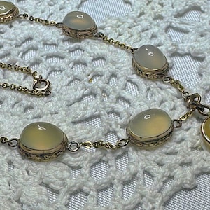 May include: A gold chain necklace with a heart-shaped pendant and oval-shaped stones. The stones are a pale yellow color.