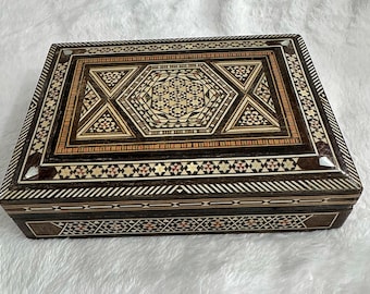 May include: A wooden box with intricate inlaid designs in shades of brown, white, and red. The box has a hinged lid and is decorated with geometric patterns.