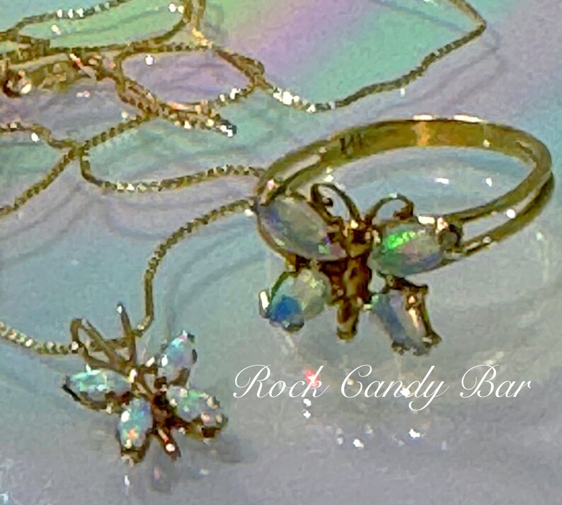 May include: Two gold necklaces with iridescent butterfly pendants. The necklaces are layered and the butterflies are different sizes. The text "Rock Candy Bar" is visible in the background.