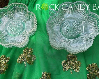 May include: Clear glass serving dishes with a flower-like design, stacked on a green surface with gold sequin shamrocks. The text "Rock Candy Bar" is visible in the image.