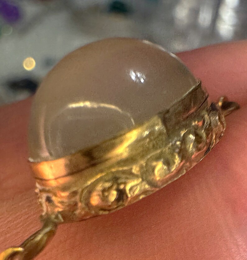 May include: A gold-toned pendant with a large, clear, round, faceted gemstone. The pendant has an ornate, detailed design around the edge.