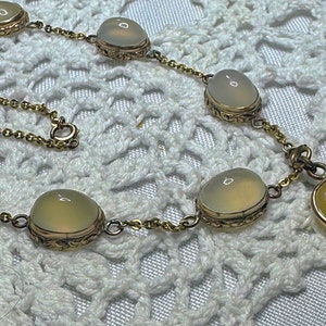 May include: A gold chain necklace with a heart-shaped pendant and oval-shaped stones. The stones are a pale yellow color.