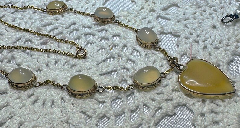 May include: A gold chain necklace with a heart-shaped pendant and oval-shaped stones. The stones are a pale yellow color.