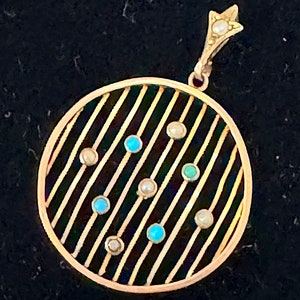 K&ouml;nnte beinhalten: Goldener Anh&auml;nger mit kreisf&ouml;rmigem Design mit parallelen Linien und abwechselnden t&uuml;rkisfarbenen und Perlenakzenten. Der Anh&auml;nger hat eine sternf&ouml;rmige Spitze mit einer Perle. Der Schmuck ist vor einem dunklen Hintergrund platziert.