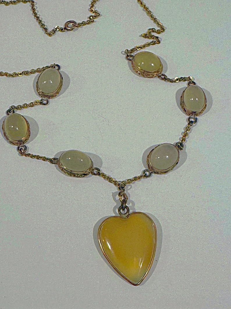 May include: A gold chain necklace with a heart-shaped pendant and oval-shaped stones. The stones are a pale yellow color.