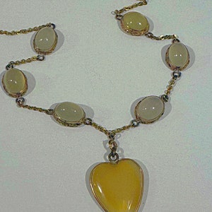 May include: A gold chain necklace with a heart-shaped pendant and oval-shaped stones. The stones are a pale yellow color.